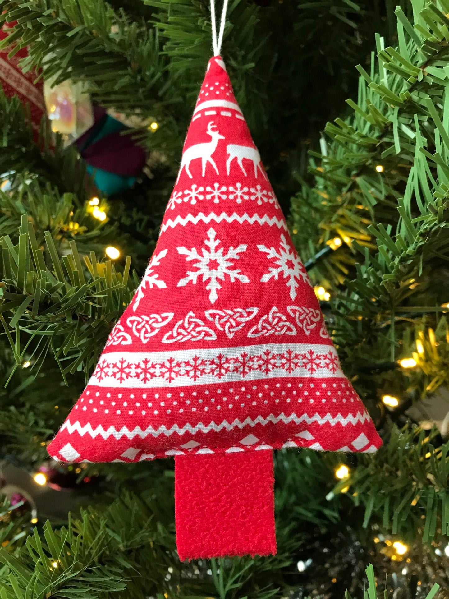 eco friendly christmas decoration handmade using upcycled fabric. Red fabric with a white scandi snowflake pattern in a tree shape.