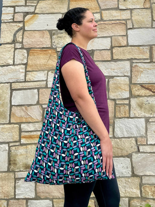 Upcycled and eco friendly fabric large tote bag worn on one shoulder by the model. Bag fabric features a geometric leaf pattern in green, white and purple on black.