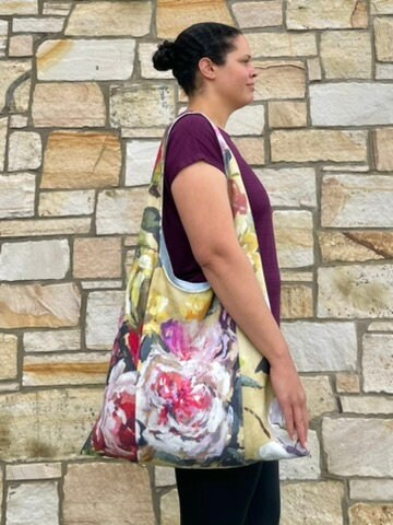 Upcycled and eco friendly linen large tote bag worn on one shoulder by the model. Bag fabric features a floral pattern with a large rose on the outer strap which is designed to hold a yoga or Pilates mat
