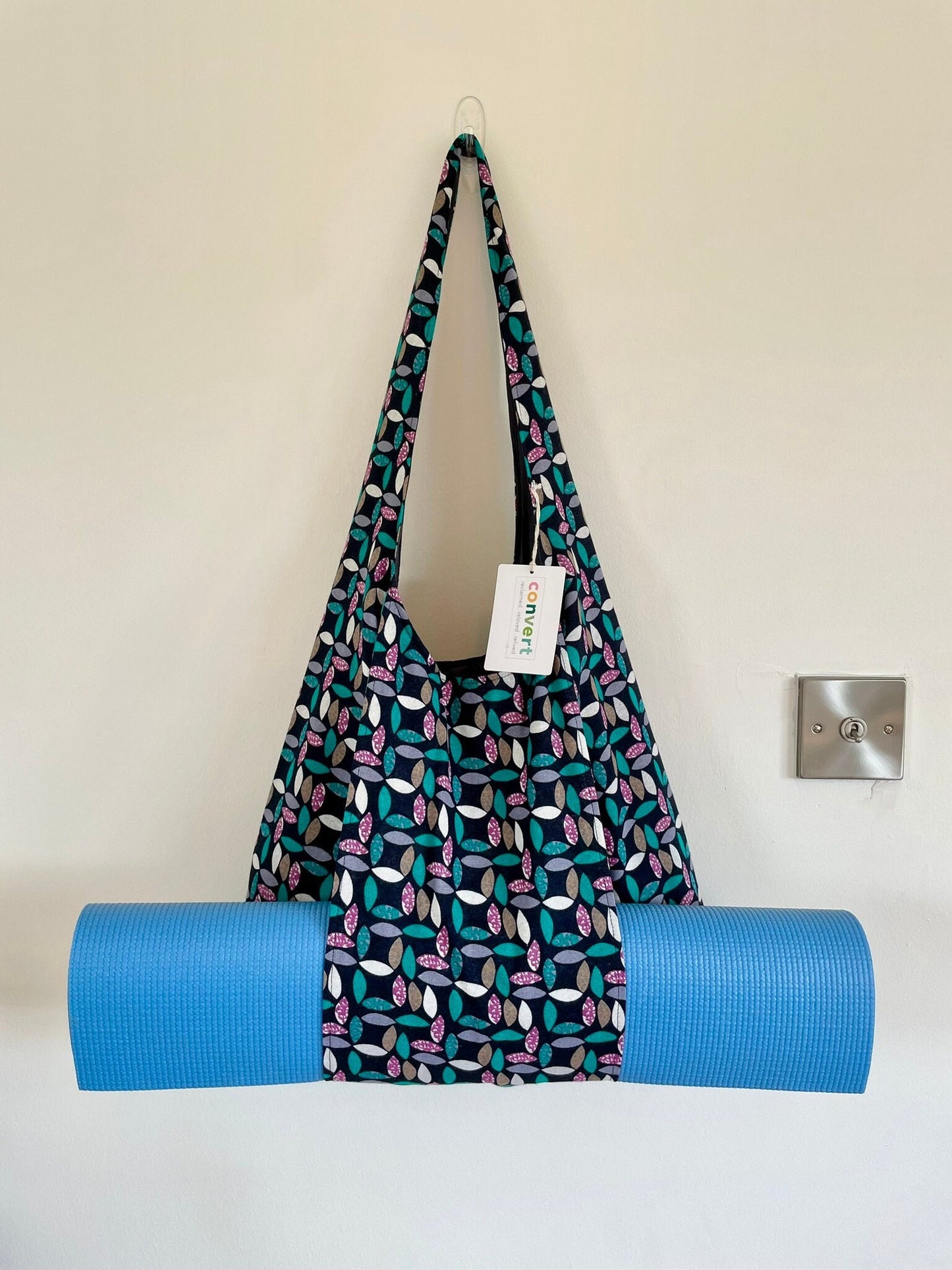 Upcycled fabric large yoga bag. Bag fabric features a geometric floral pattern in white, green and purple on black. The outer strap holds a rolled yoga or Pilates mat