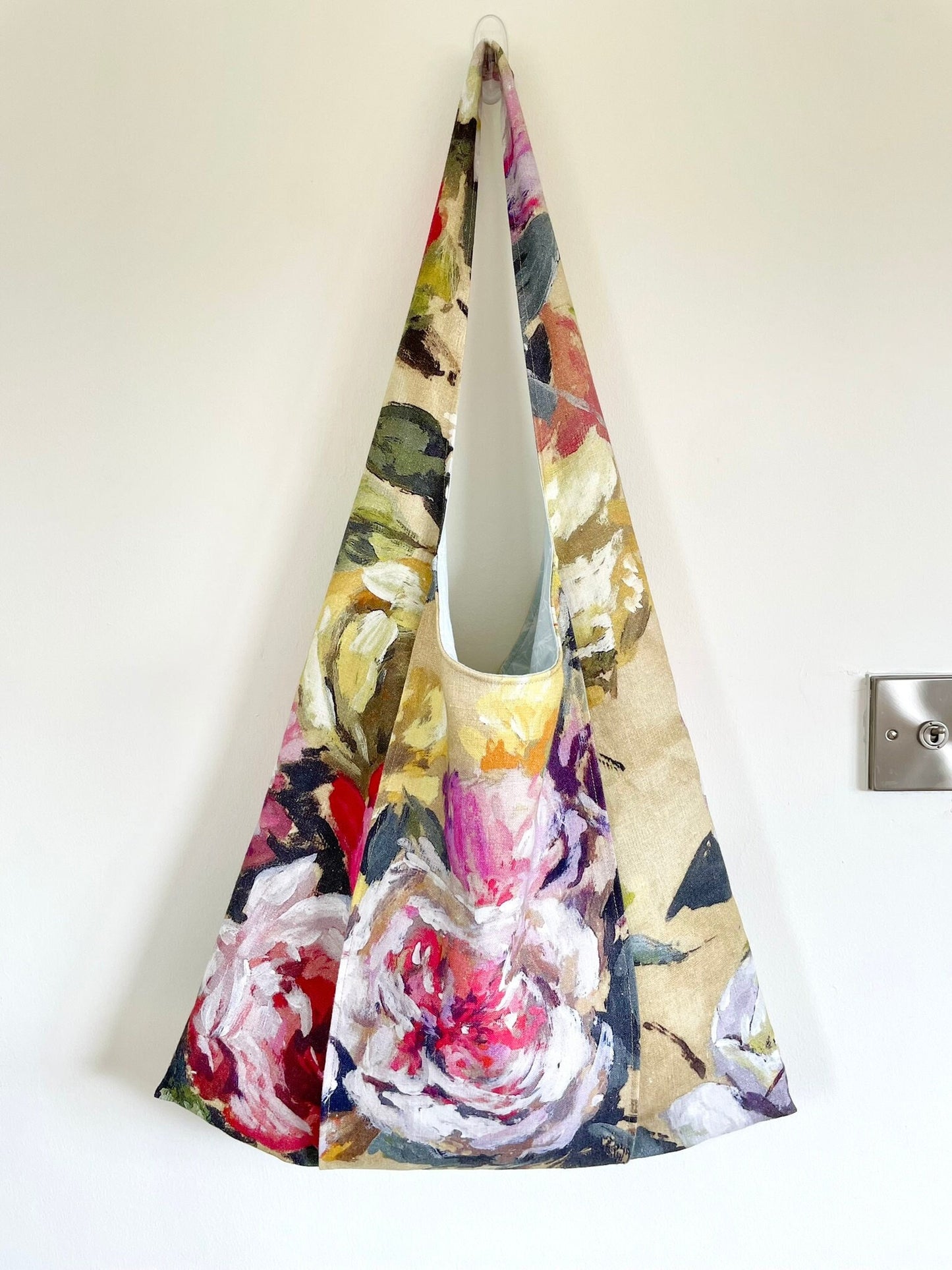 Upcycled linen large floral shoulder bag worn. Bag fabric features a floral pattern with a large rose on the outer strap which is designed to hold a yoga or Pilates mat