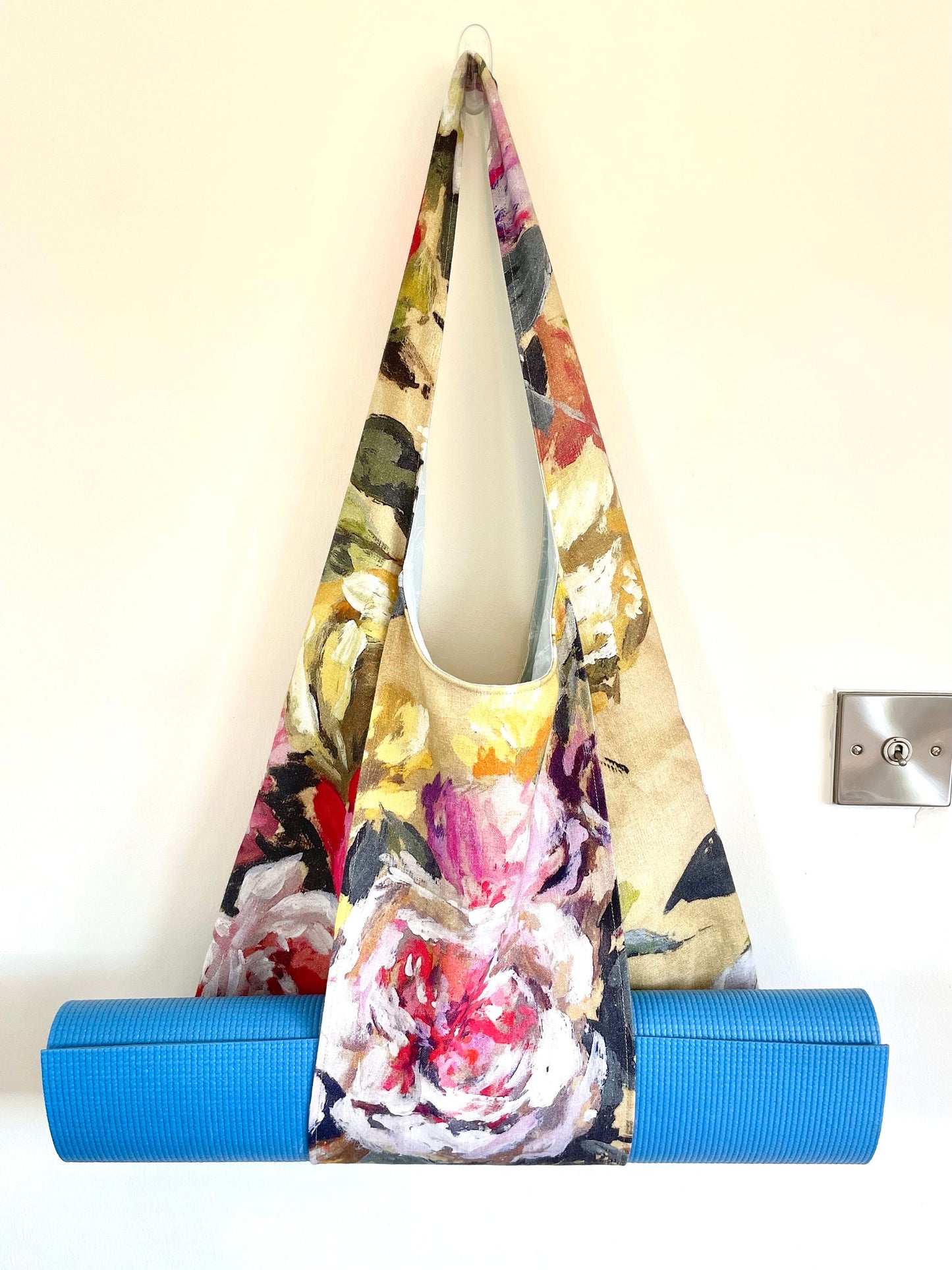 Upcycled yoga mat bag in floral linen fabric handmade in Ireland. Bag shows a rolled yoga mat being held horizontally by a large outer strap.