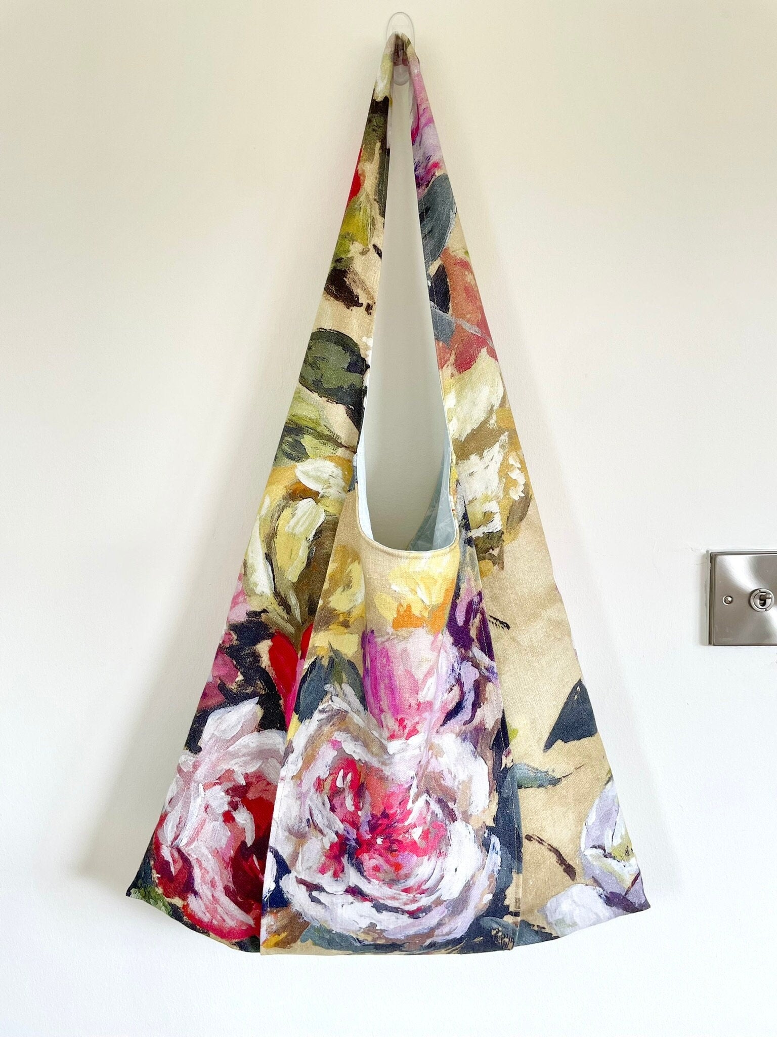 Upcycled linen large floral shoulder bag worn. Bag fabric features a floral pattern with a large rose on the outer strap which is designed to hold a yoga or Pilates mat