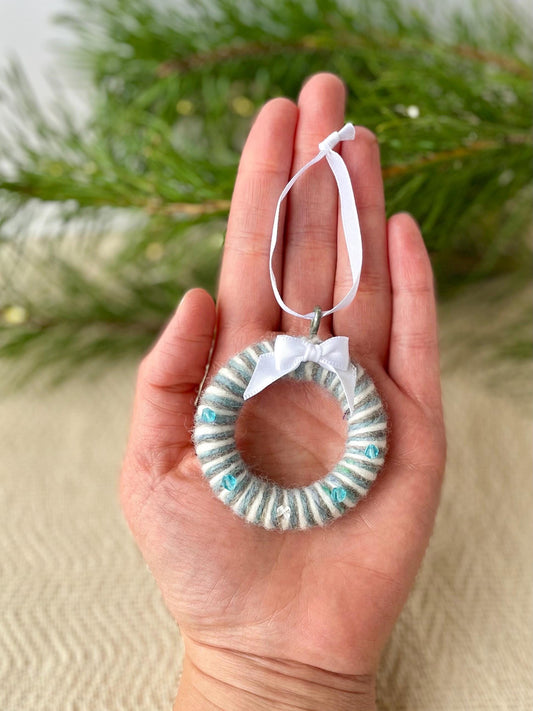 Blue, grey and white wool upcycled christmas decoration handmade in Ireland. The piece is in a circular wreath shape and is finished with blue glass beads and white ribbon.